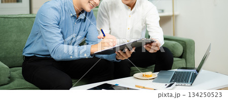 Two Asian businessmen smiling while signing a contract on clipboard, symbolizing business cooperation, teamwork Two Asian businessmen smiling while signing a contract on clipboard, symbolizing business cooperation, teamwork 134250523