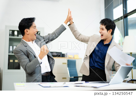 Two excited businessmen cheering with joy in office after success. Concept of teamwork, business win Two excited businessmen cheering with joy in office after success. Concept of teamwork, business win 134250547
