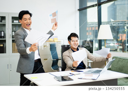 Two excited businessmen cheering with joy in office after success. Concept of teamwork, business win Two excited businessmen cheering with joy in office after success. Concept of teamwork, business win 134250555