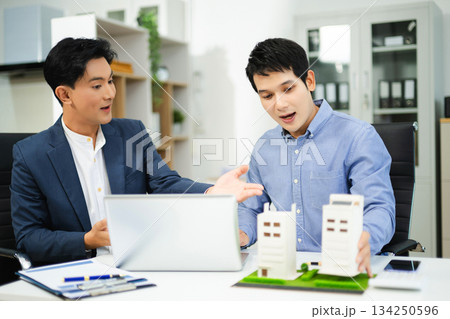 Two businessmen discuss and sign a real estate contract with housing models on a desk for concepts of property, investment Two businessmen discuss and sign a real estate contract with housing models on a desk for concepts of property, investment 134250596