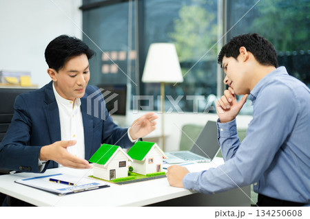Real estate agent consulting with buyer on house model and pricing using calculator in modern office. and client service. Real estate agent consulting with buyer on house model and pricing using calculator in modern office. and client service. 134250608
