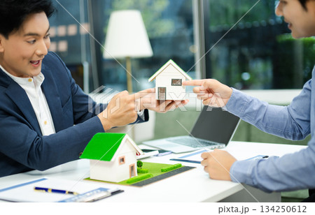 Real estate agent consulting with buyer on house model and pricing using calculator in modern office. and client service. Real estate agent consulting with buyer on house model and pricing using calculator in modern office. and client service. 134250612