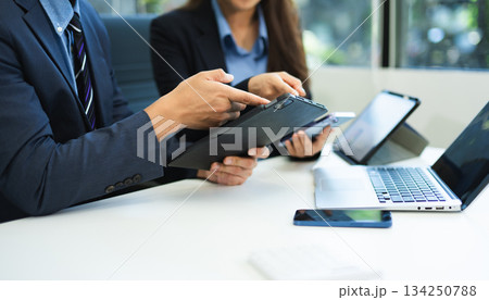 Business documents on office table with smart phone and laptop and two colleagues discussing data in the background Business documents on office table with smart phone and laptop and two colleagues discussing data in the background 134250788