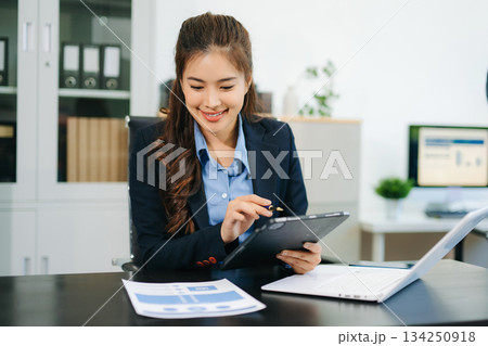 Asian woman with a smile standing holding notepad and tablet at the modern office. Asian woman with a smile standing holding notepad and tablet at the modern office. 134250918