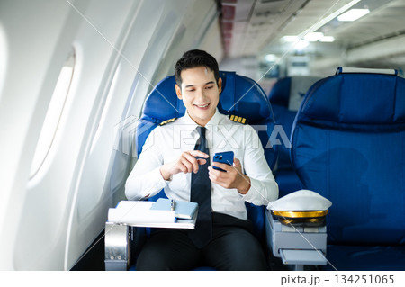 Confident pilot in uniform using smartphone in airplane cabin, ideal for aviation, communication, and travel lifestyle stock imagery. Confident pilot in uniform using smartphone in airplane cabin, ideal for aviation, communication, and travel lifestyle stock imagery. 134251065