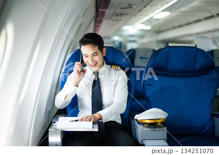 Confident airline pilot in uniform using wireless earbuds while reviewing documents, perfect for aviation, travel, and modern communication themes Confident airline pilot in uniform using wireless earbuds while reviewing documents, perfect for aviation, travel, and modern communication themes 134251070