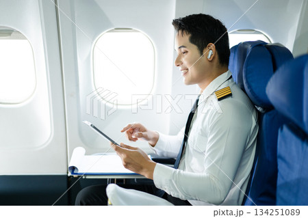 Confident pilot in uniform using smartphone in airplane cabin, ideal for aviation, communication, and travel lifestyle stock imagery. 134251089