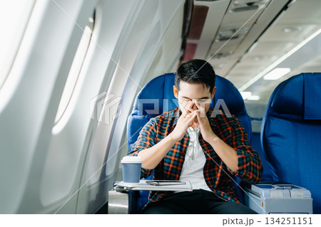 Travel stress, jet lag, or motion sickness. Young man with a headache or fatigue during a long flight. Tired passenger on a business trip. Travel stress, jet lag, or motion sickness. Young man with a headache or fatigue during a long flight. Tired passenger on a business trip. 134251151