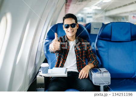 Happy young traveler celebrating victory with a fist pump on the airplane. Business success, achievement, and excited travel journey. Win, style, phone, tech. Happy young traveler celebrating victory with a fist pump on the airplane. Business success, achievement, and excited travel journey. Win, style, phone, tech. 134251196