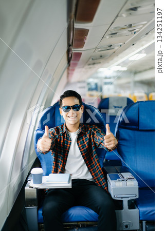 Happy young traveler celebrating victory with a fist pump on the airplane. Business success, achievement, and excited travel journey. Win, style, phone, tech. Happy young traveler celebrating victory with a fist pump on the airplane. Business success, achievement, and excited travel journey. Win, style, phone, tech. 134251197