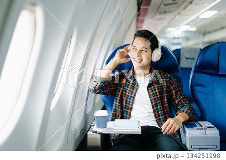 Happy man in a plane seat. Diverse travel series: work, talk, call, listen, read, stress, and joy on a long flight. Tech, mobile, and view are key parts of the trip. 134251198