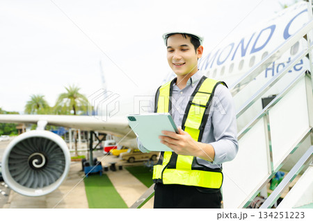 Ground crew engineer in safety vest and helmet pointing and holding documents during airplane inspection, perfect for aviation and flight safety themes 134251223