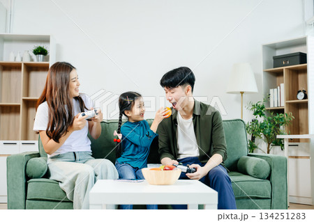 Happy Asian parents and child bonding, playing games, laughing, and enjoying social media together in cozy living room. Family time, love Happy Asian parents and child bonding, playing games, laughing, and enjoying social media together in cozy living room. Family time, love 134251283