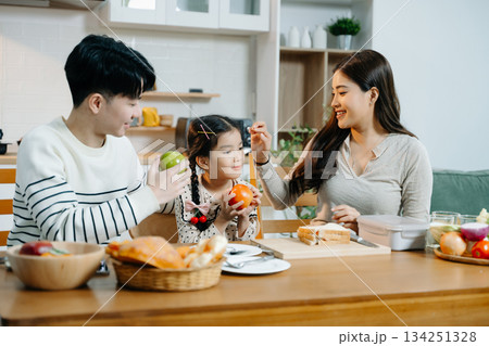 Asian family shares a happy morning, preparing and enjoying breakfast in a cozy kitchen. Parents and daughter bond over love 134251328