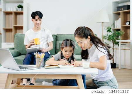 Asian parents cheering and guiding daughter through homework at home. Joyful teamwork, love, and learning in a cozy, 134251337