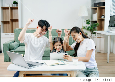 Asian parents cheering and guiding daughter through homework at home. Joyful teamwork, love, and learning in a cozy, Asian parents cheering and guiding daughter through homework at home. Joyful teamwork, love, and learning in a cozy, 134251341