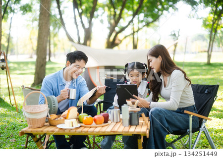 Joyful Asian family camping in a sunny garden, bonding over BBQ, tech, and laughter. Parents and daughter enjoy outdoor Joyful Asian family camping in a sunny garden, bonding over BBQ, tech, and laughter. Parents and daughter enjoy outdoor 134251449