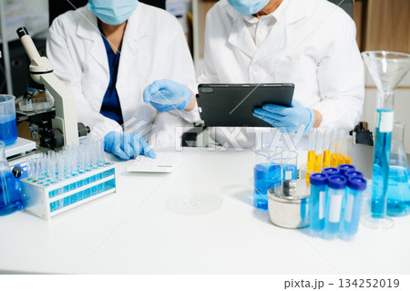 scientists in lab coats conducting research, handling glassware, and working with chemicals 134252019