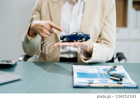 Business professionals finalize a car sale agreement with paperwork and model car, capturing themes 134252191