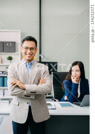 Young attractive Asian male office worker business suits smiling at camera in office Young attractive Asian male office worker business suits smiling at camera in office 134252371