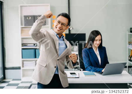 Young attractive Asian male office worker business suits smiling at camera in office Young attractive Asian male office worker business suits smiling at camera in office 134252372