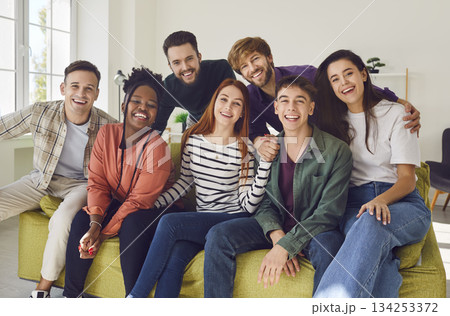 Portrait of smiling happy diverse friends group sitting on sofa at home and looking at camera. 134253372