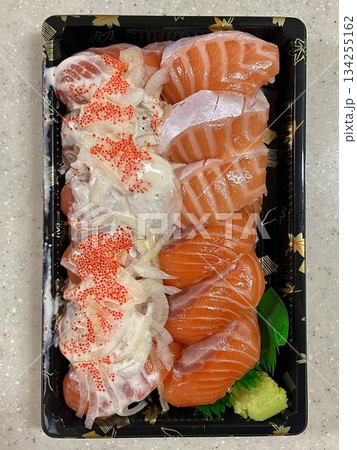 Fresh salmon sushi with bright orange slices placed on top of perfectly shaped rice, garnished with green leaves and radish for a simple, colorful, and appetizing presentation 134255162