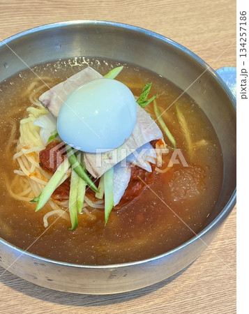 Naengmyeon, a refreshing Korean cold noodle dish served in an icy broth, topped with sliced vegetables, a boiled egg, and spicy sauce. Perfect for summer food photography and Korean cuisine projects. 134257186