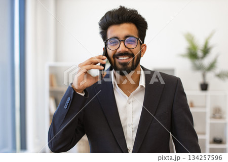 An Indian businessman smiles while talking on his cell phone in an office setting An Indian businessman smiles while talking on his cell phone in an office setting 134257596
