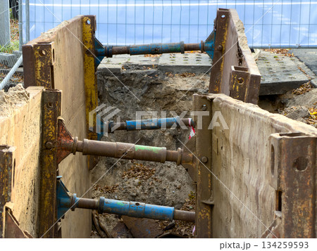 Robust metal trench shoring system with rusty panels and adjustable struts secures a deep excavation ditch, vital for construction safety and infrastructure projects 134259593