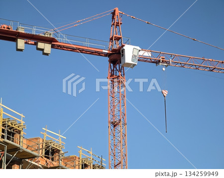 construction crane action, lifting operations underway under clear blue sky at bustling building construction crane action, lifting operations underway under clear blue sky at bustling building 134259949