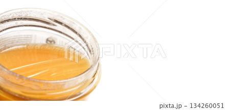 Glass jar with amber coloured honey, closeup detail, isolated on white background, space for text right side Glass jar with amber coloured honey, closeup detail, isolated on white background, space for text right side 134260051