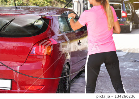 Young woman washing her red car in self serve carwash, view from back 134260236