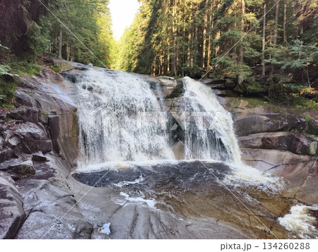 vigorous waterfalls cascade onto rugged stones, dynamic river descent over granite with frothy whitewater 134260288