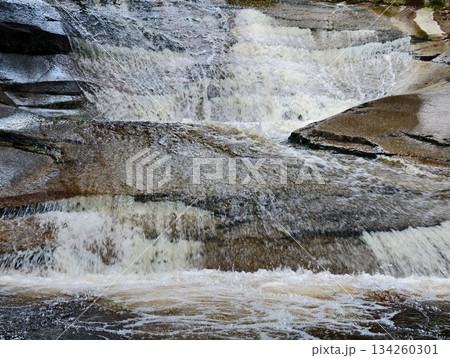 peaceful waterfall over rocks, calm waterfall descending over polished stone surfaces with haze 134260301