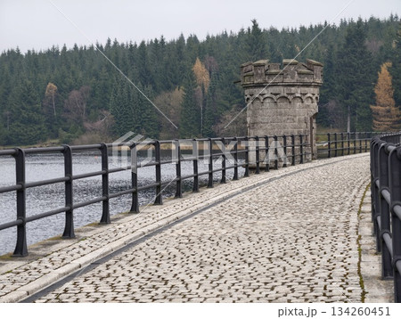 serene damside stone passageway, calm pathway beside reservoir with rustic architectural features 134260451