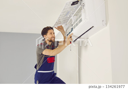 Portrait of smiling electrician with screwdriver maintaining air conditioner indoors. 134261977