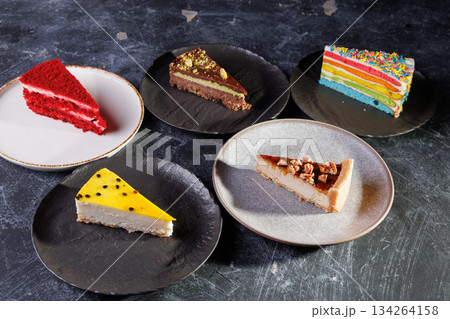 Assorted Cake Slices On Dark Slate Plates Create Colorful Dessert Display For Party 134264158