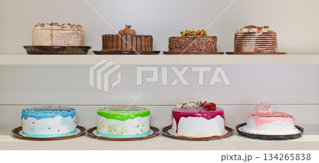 A row of cakes on a shelf, with one cake being pink 134265838