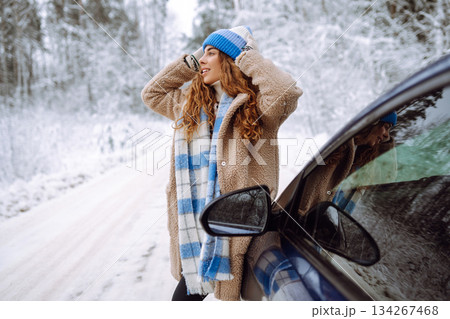 Beautiful young woman near a car in a snowy forest. First snow, great mood. Concept of vacation. Beautiful young woman near a car in a snowy forest. First snow, great mood. Concept of vacation. 134267468
