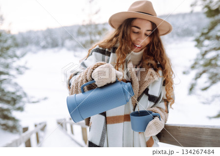 Young woman drinks hot tea while holding a thermos in nature. . Vacation concept Young woman drinks hot tea while holding a thermos in nature. . Vacation concept 134267484
