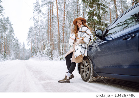 Beautiful young woman near a car in a snowy forest. First snow, great mood. Concept of vacation. 134267496