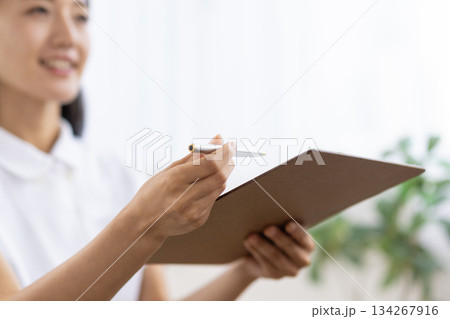 白衣を着た女性が手に持つバインダーとペンのクローズアップ 134267916