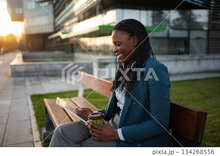 Businesswoman enjoying coffee and tablet outdoors in city 134268556