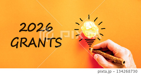 2026 Grants symbol. Concept words 2026 Grants on beautiful orange paper. Beautiful orange paper background. Light bulb icon. Businessman's hand with pen. Business and 2026 grants concept. Copy space. 134268730