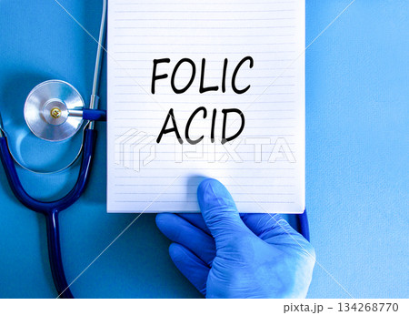 Folic acid symbol. Concept words Folic acid on beautiful white note. Doctor's hand in blue medical glove. Stethoscope. Beautiful blue background. Medical healthy lifestyle folic acid concept. Folic acid symbol. Concept words Folic acid on beautiful white note. Doctor's hand in blue medical glove. Stethoscope. Beautiful blue background. Medical healthy lifestyle folic acid concept. 134268770