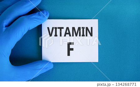 Vitamin F symbol. Concept words Vitamin F on beautiful white card. Doctor's hand in blue medical glove. Beautiful blue background. Medical healthy lifestyle Vitamin F concept. Vitamin F symbol. Concept words Vitamin F on beautiful white card. Doctor's hand in blue medical glove. Beautiful blue background. Medical healthy lifestyle Vitamin F concept. 134268771