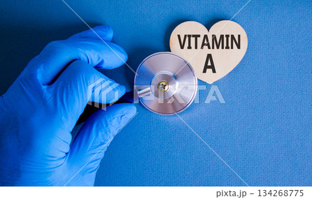 Vitamin A symbol. Concept words Vitamin A on beautiful wooden heart. Doctor's hand in blue medical glove. Stethoscope. Beautiful blue background. Medical healthy lifestyle Vitamin A concept. 134268775