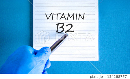 Vitamin B2 riboflavin symbol. Concept words Vitamin B2 on beautiful white note. Doctor's hand in blue medical glove. Beautiful blue background. Medical healthy lifestyle Vitamin B2 riboflavin concept. 134268777