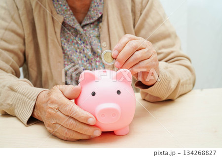 Retired elderly woman putting coins money in piggy bank and worry about monthly expenses and treatment fee payment. 134268827